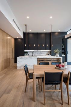 an open kitchen and dining room with wood flooring, black cabinets and marble countertops