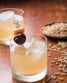 two glasses filled with alcoholic drinks on top of a wooden table next to oatmeal