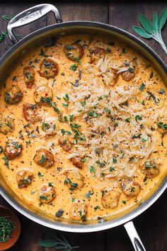 a pan filled with pasta and mushrooms on top of a wooden table next to spoons