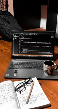 an open laptop computer sitting on top of a wooden table next to a cup of coffee