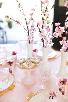 the table is set with pink flowers and desserts