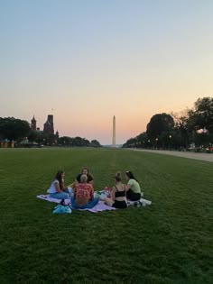 four people sitting on a blanket in the middle of a grassy field with washington monument in the background