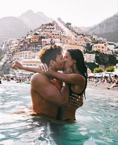 a man and woman are in the water near a mountain town with houses on it