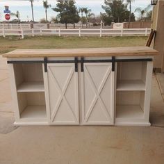 a white kitchen island with sliding doors on the top and bottom, in front of a fence