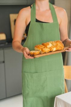 a woman in an apron holding a tray of bread