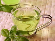 a glass cup filled with green tea next to some leaves