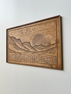 a wooden wall hanging on the side of a building with mountains and sun in it