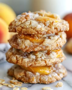 three cookies stacked on top of each other with oats scattered around them and peaches in the background