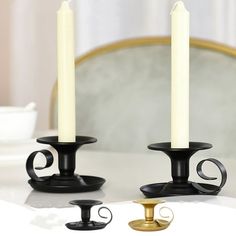 two black candles sitting on top of a white table next to a gold candle holder