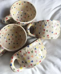 four ceramic cups and saucers with hearts painted on them are sitting on a white sheet