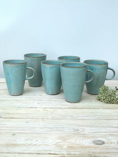 five teal mugs sitting on top of a wooden table next to a plant