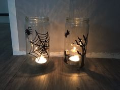 two mason jars with candles in them sitting on a wooden floor next to a wall