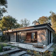 an outdoor patio with stone walls and seating area in the foreground, surrounded by greenery