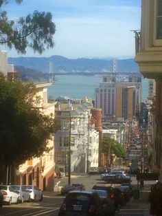 a city street with cars parked on both sides and the bay bridge in the background