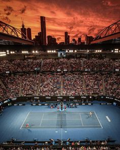 a tennis match is being played in front of a large crowd at sunset with the sun going down