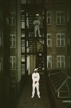 a man standing in front of a tall building next to another person wearing a white suit