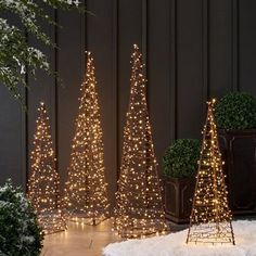 three small christmas trees are lit up in front of a black wall with snow on the ground