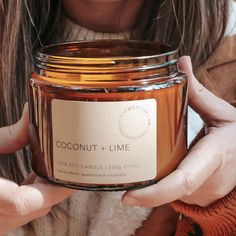 a woman holding a jar of coconut + lime candle in front of her face and hands