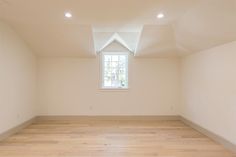 an empty room with white walls and wood flooring in the center is a window