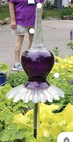 a man standing next to a purple and white glass water fountain in the middle of flowers