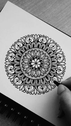 a person is drawing on paper with a pen and inking it in the shape of a flower