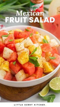 a white bowl filled with fruit salad next to sliced watermelon and limes