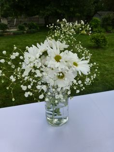 a vase filled with white flowers sitting on top of a table next to a field