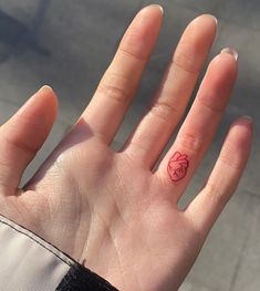 a person's hand with a small red heart tattoo on their left thumb and finger