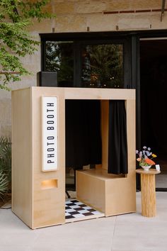 a wooden booth with black curtains on the front and side doors, in front of a building