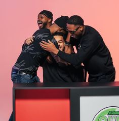 three men hugging each other while standing on top of a table with a pink background