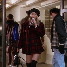 a woman in plaid coat and black hat drinking from a bottle while standing next to other people