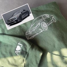 an image of a car on a green shirt with white writing and a sticker next to it