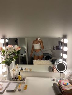 a woman taking a selfie in front of a mirror with flowers and cosmetics on the counter