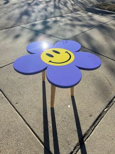 a purple flower with a smiley face painted on it sitting in the middle of a sidewalk