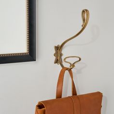 a brown purse hanging from a hook on the wall next to a framed photo and mirror