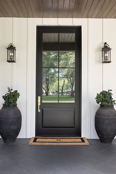 two large vases with plants are on the front porch next to a black door