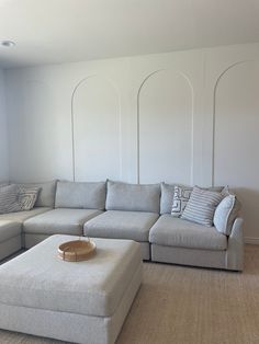 a couch and ottoman in a room with white walls, beige carpet and rugs on the floor