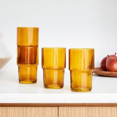 an assortment of yellow glassware on a white counter top with apples in the background