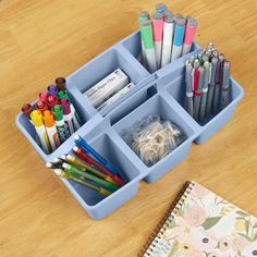 a blue container filled with lots of different colored markers and pencils on top of a wooden table