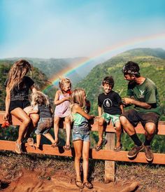 a group of people sitting on top of a wooden bench next to a rainbow in the sky