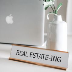 a real estate - ing sign sitting next to an apple laptop on a white desk