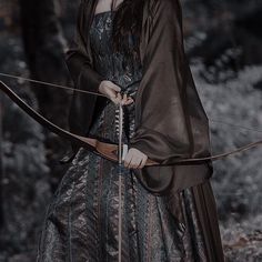 a woman dressed in medieval clothing holding a bow and arrow while standing in the woods