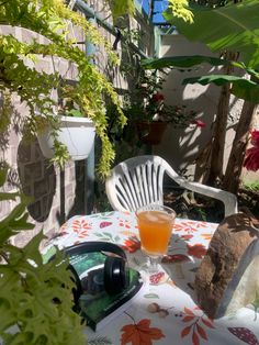 an orange drink sitting on top of a table next to a white chair and potted plant