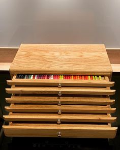 a wooden box filled with colored pencils on top of a table next to a wall