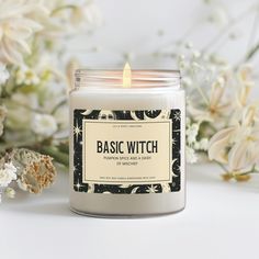 a candle sitting on top of a white table next to some flowers and plants with the words basic witch written on it