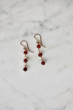 Sweet and dainty, these minimalist gold filled earrings with garnet beads are perfect for everyday wear. The earrings feature tiny faceted pomegranate red garnet beads, dangling from 14k gold filled ear wires.  These cute earrings will look great whether you are heading to a day at work or an evening out. Made using the highest quality USA and UK sourced materials. About Garnet: Garnet has been used as a gemstone for over 5000 years. It has been found in the jewelry of many Egyptian burials and Tiny Gemstone Earrings, Rome Antique, Gemstone Drop Earrings, Gold Dangle Earrings, January Birthstone, Garnet Earrings, Earrings Dainty, Gold Filled Earrings, Red Earrings