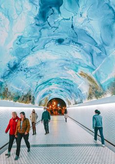 people are walking through an ice covered tunnel in the winter, with blue and white marble on the ceiling