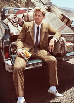 a man in a suit sitting on the back of a pick up truck with luggage