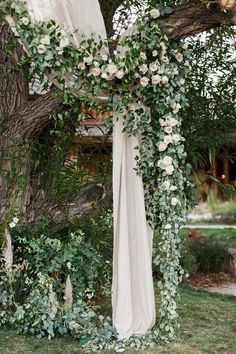 an outdoor wedding ceremony setup with white flowers and greenery on the arbor, in front of a tree