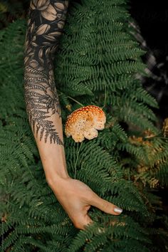 a person's arm with tattoos on it and a mushroom in the grass next to them